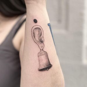 Detailed illustrative design on forearm by Mané, featuring a bell and ear motif in bold blackwork style.