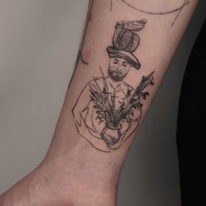Discover Mané's stunning blackwork design featuring a bird, flower, hat, and vase on the forearm. A truly unique piece of art!