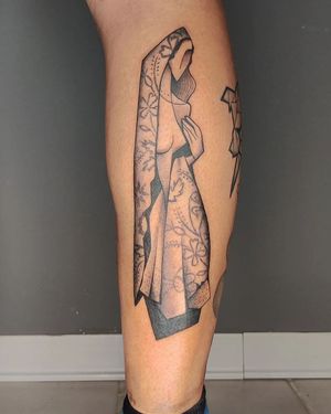 Elegant blackwork tattoo on lower leg featuring a beautiful flower and a woman designed by Baingio. Intricate patterns and detailed illustration.