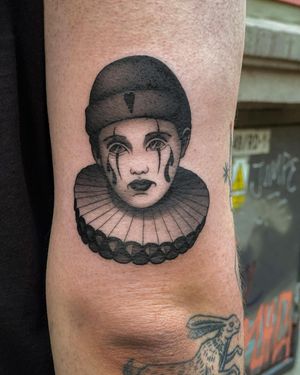 Unique blackwork tattoo by Joanna featuring a heart, pattern, clown, and cap on the upper arm.