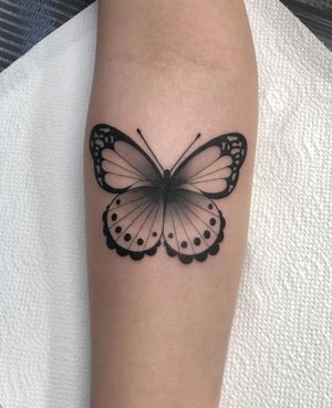 Elegant blackwork butterfly design on forearm by Joanna, featuring fine line details and illustrative style.