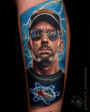 Unique lower leg tattoo featuring realistic portrait of Hugh Laurie with illustrative elements of man, cap, glasses, and house. By Slava.