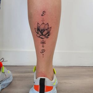 Elegant blackwork tattoo by Dorota featuring a delicate lotus flower and small lettering on the lower leg.