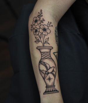 Stunning blackwork forearm tattoo featuring a bird, flower, and vase, by tattoo artist ALEJANDRO.