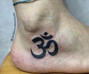 Símbolo OM tatuado abaixo do tornozelo, representa o som e a vibração que deu origem à Criação.
