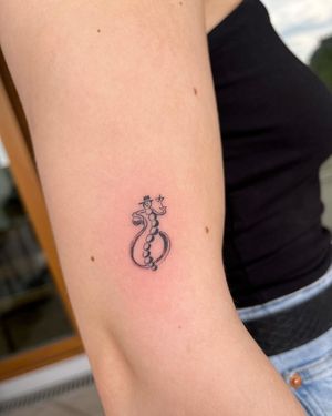 This elegant tattoo features a hat, glass, and drink motif on the upper arm, beautifully executed by tattoo artist Sofi.