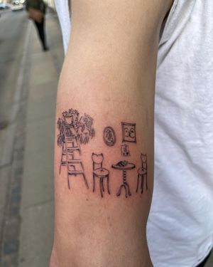 This illustrative forearm tattoo by Sofi features a delicate flower, ladder, chair, table, and photo in fine line style.