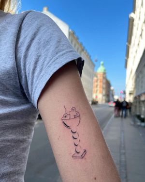 Illustrative upper arm tattoo featuring a man with a cigarette behind a glass motif, by Sofi.
