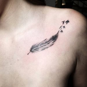 Beautiful illustrative tattoo featuring a bird and feather motif on the chest, done by the talented artist Shasza.