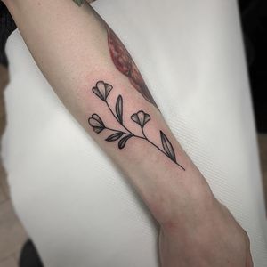 A delicate fine line flower design by Rachel Angharad, perfect for a sophisticated and timeless look on your forearm.