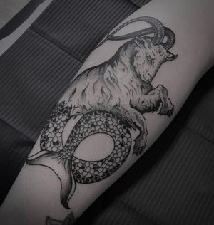 This blackwork forearm tattoo by Shasza features a unique combination of a majestic goat and enchanting mermaid design.