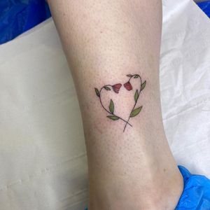 Delicate ankle tattoo by Rachel Angharad featuring a detailed flower and heart design in fine line illustrative style.