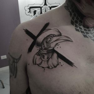 Impressive blackwork style tattoo featuring a cross, dr plague, and a hat by Shasza. A hauntingly beautiful piece for your chest.