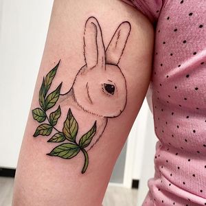 Get inked by Rachel Angharad with this illustrative tattoo featuring a rabbit surrounded by a delicate sprig and leaf design on your upper arm.
