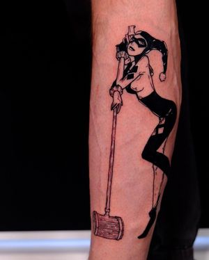Blackwork forearm tattoo featuring iconic Harley Quinn motifs - gun and hammer, created by Denis in an illustrative style.