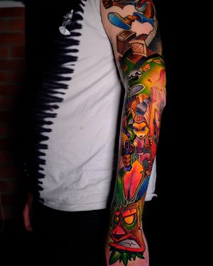 This vibrant sleeve tattoo features a new school style with illustrations of a gun, alien, box, and Crash Bandicoot, all expertly done by artist Denis.