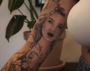 Elegant black and gray arm tattoo by Liliia, featuring a detailed depiction of a flower and a woman in illustrative style.