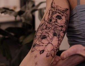 Get a stunning blackwork upper arm tattoo of an owl and flower by the talented artist Liliia.