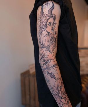 A striking blackwork sleeve tattoo featuring ornamental elements and an illustrative design of a woman with devil horns and earrings.