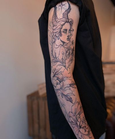 A striking blackwork sleeve tattoo featuring ornamental elements and an illustrative design of a woman with devil horns and earrings.