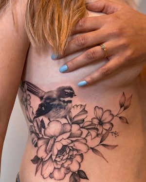 Get a stunning blackwork tattoo of a bird and flower on your ribs, created by the talented artist Liliia.