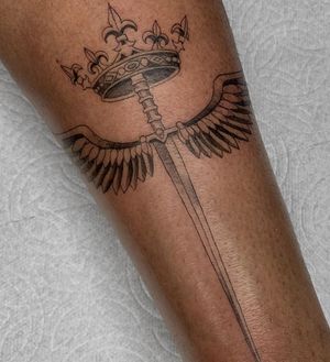 Elegant blackwork design on forearm featuring a sword, crown, and wings by artist Angel Chavez.