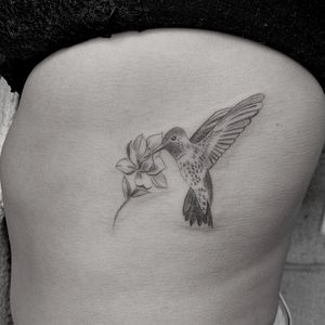 Beautiful blackwork tattoo of a hummingbird and flower on the ribs by Angel Chavez. Unique and intricate illustrative design.