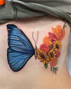 Beautiful rib tattoo by Michaelle Fiore featuring a butterfly, flower, and sunflower in vibrant watercolor style.