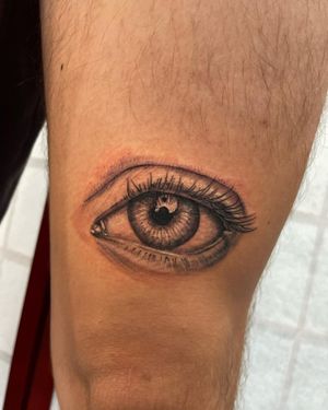 Get mesmerized by Michaelle Fiore's incredible illustrative eye tattoo design on your upper leg. Experience the power and depth of realism in this stunning art piece.
