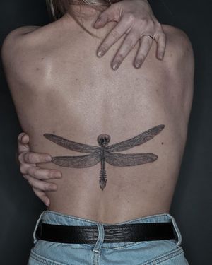 Bold blackwork design by Toma featuring a dragonfly and skull, perfect for back placement. Unleash your inner edge with this stunning piece.