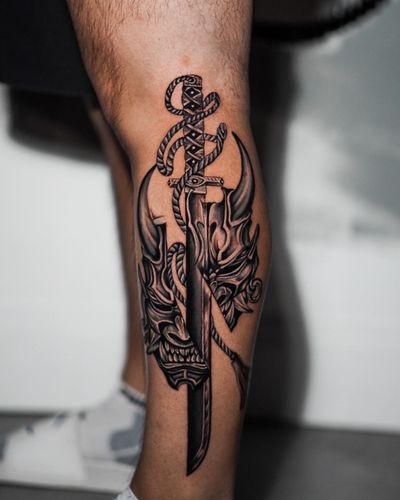 Get a striking blackwork illustration of a sword and hannya mask by talented artist Dorota on your lower leg.