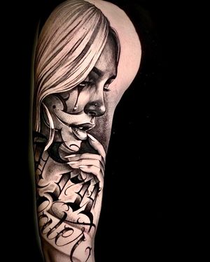 Get this bold blackwork tattoo featuring a woman, clown, tears, and a powerful quote by the talented artist Mika on your upper arm.