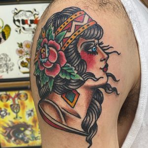 Vibrant neo-traditional tattoo by Jason Fancher featuring a beautiful woman with earrings surrounded by intricate flowers on the upper arm.