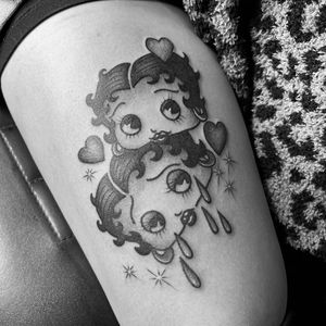 This blackwork illustrative tattoo on the upper leg features Betty Boop with a heart motif, tears, earrings, and a woman motif. Designed by the talented artist Kat Freedman.