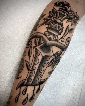 This blackwork tattoo by Sasha Ignarski features a striking design of flowers, a dagger, and intricate patterns on the forearm.