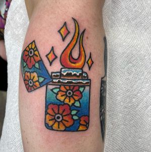Vibrant neo-traditional design by Jason Fancher featuring a beautiful flower and dynamic flames engulfing a lighter on the arm.
