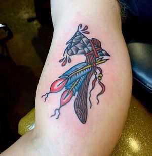 Illustrative arm tattoo by Kat Freedman blending feather and axe motifs in neo-traditional style.