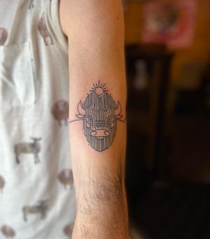 Get a bold illustrative tattoo by Kat Freedman featuring a sun, pattern, and bull on your upper arm. Perfect for those who love unique blackwork designs.