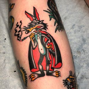 A unique tattoo by Nick Osbourn featuring a coyote wearing a cape and smoking a cigarette, beautifully illustrated on the lower leg.