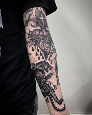 This stunning blackwork tattoo by Philip LaRocca combines a fierce panther, heart, cross, hannya mask, and thorns for a striking and meaningful design.