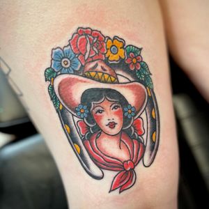 Traditional style tattoo on upper leg featuring a woman wearing a hat surrounded by flowers, expertly done by Kat Freedman.