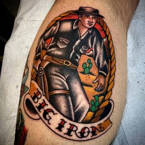Capture the spirit of the Wild West with this traditional style lower leg tattoo featuring a gun-wielding cowboy, man in a hat, and a powerful quote. Designed by Sasha Ignarski.
