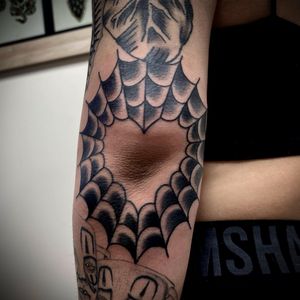 Illustrative blackwork tattoo of a spider, heart, and spider web on the arm by Sasha Ignarski.