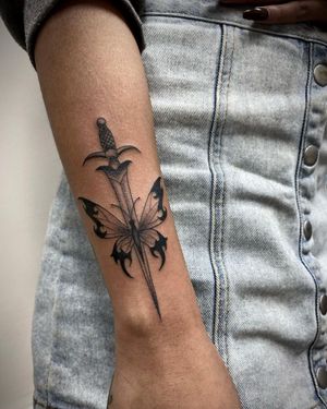 Beautiful blackwork tattoo by Sasha Ignarski featuring a detailed butterfly and dagger design on the forearm.