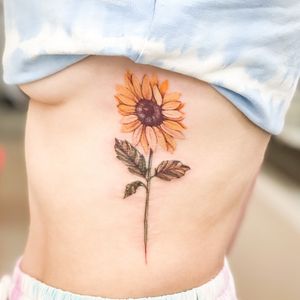 Beautiful sunflower tattoo on ribs by artist Juliany Braga, featuring detailed illustrative style.