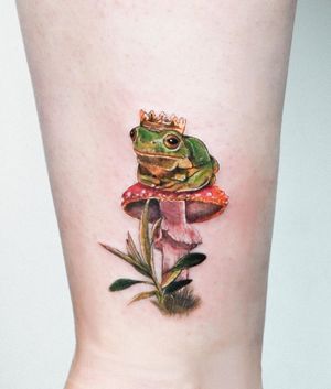 Captivating realism tattoo featuring a frog with a crown, mushroom, and leaf, expertly done by Juliany Braga.