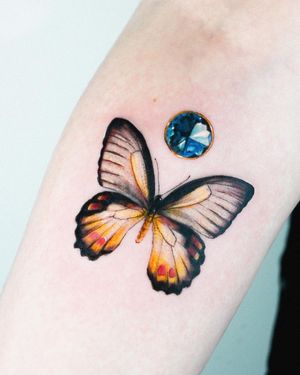 Experience the beauty of Juliany Braga's illustrative style with this stunning forearm tattoo featuring a butterfly, crystal, and earrings design. Perfect for those who love realism tattoos.