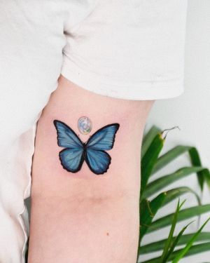 A beautiful butterfly tattoo on the upper arm, expertly done in an illustrative style by the talented artist Juliany Braga.