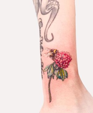 Capture the beauty of nature with this stunning illustrative tattoo featuring a bee and flower design by Juliany Braga.