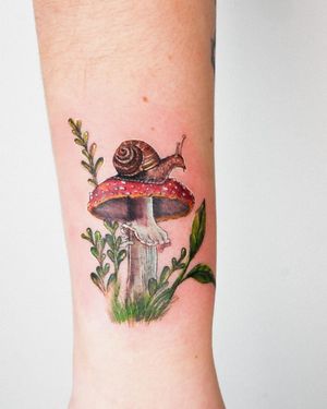 An enchanting neo-traditional tattoo featuring a snail, mushroom, and leaf, expertly done by Juliany Braga.
